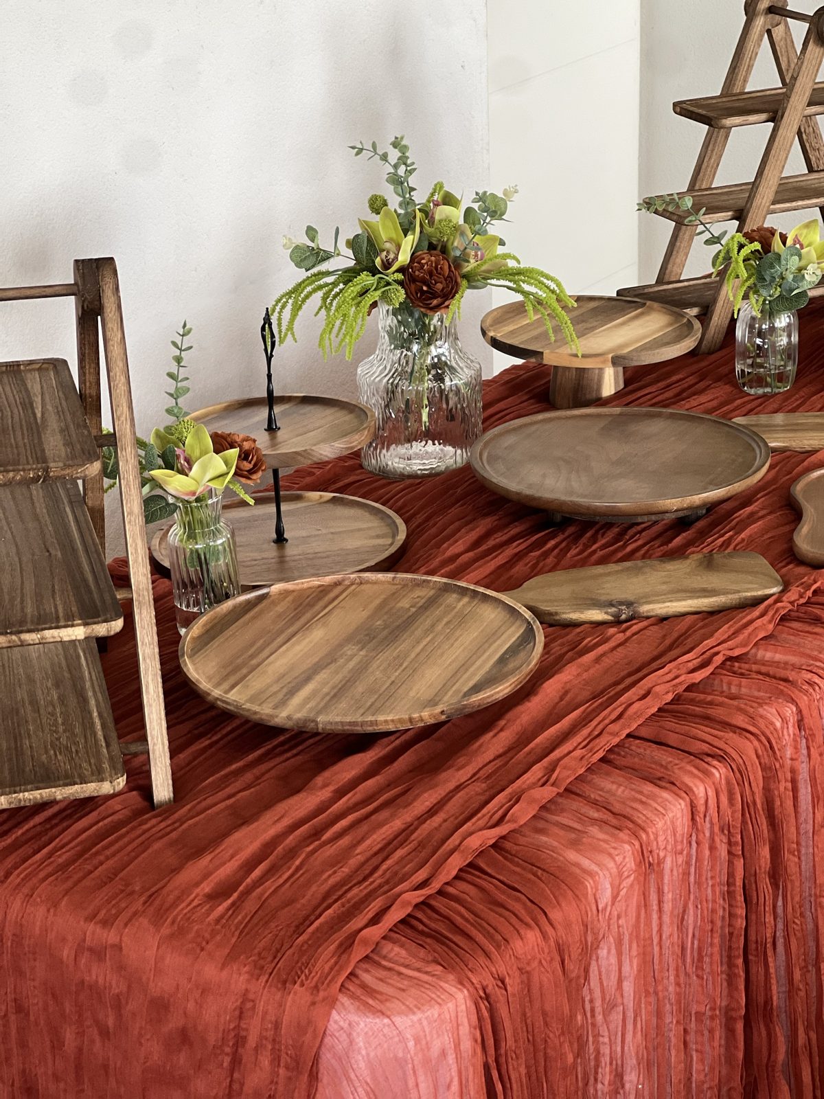 Buffet bois naturel sur chemin de table terracotta : échelles, plateaux en acacia et fleurs